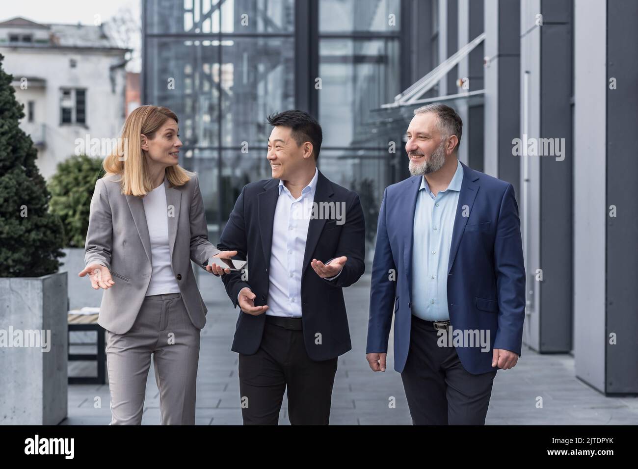 Diverse business group, three male and female workers walking and chatting discussing plans, outside office building Stock Photo