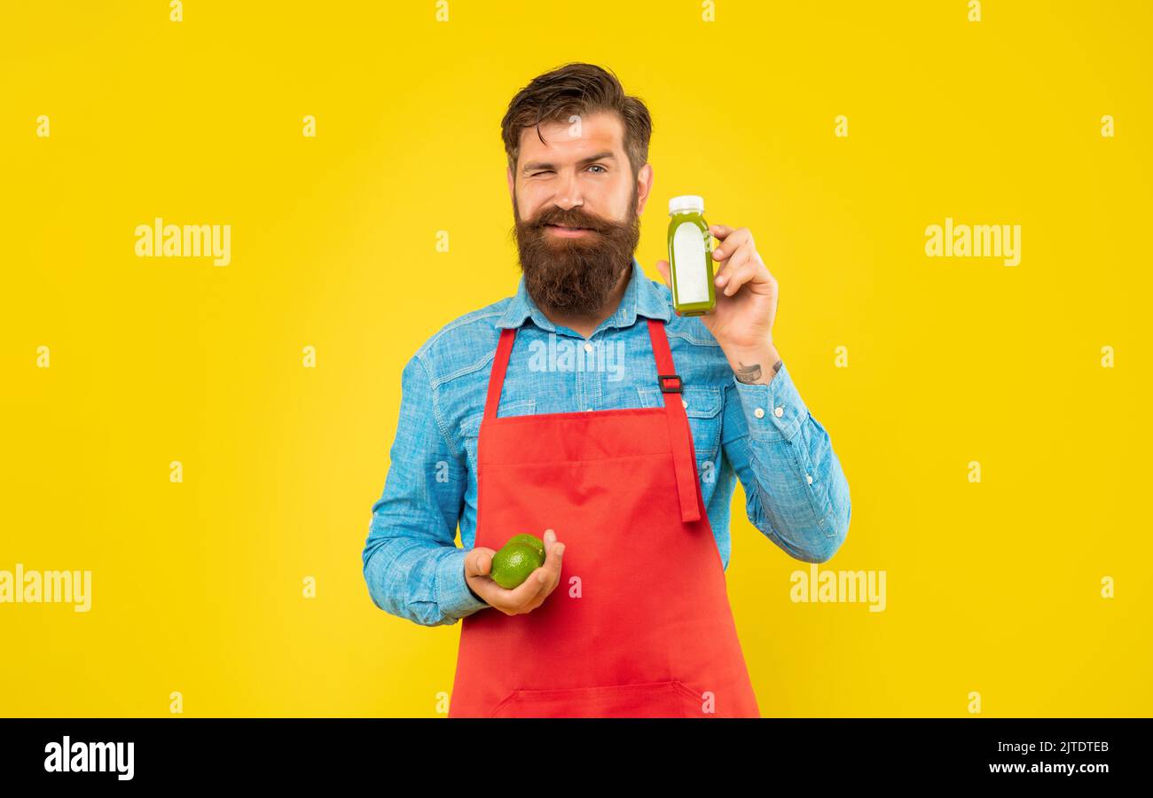 Winking man in apron holding limes and juice bottle yellow background, juice barkeeper Stock Photo