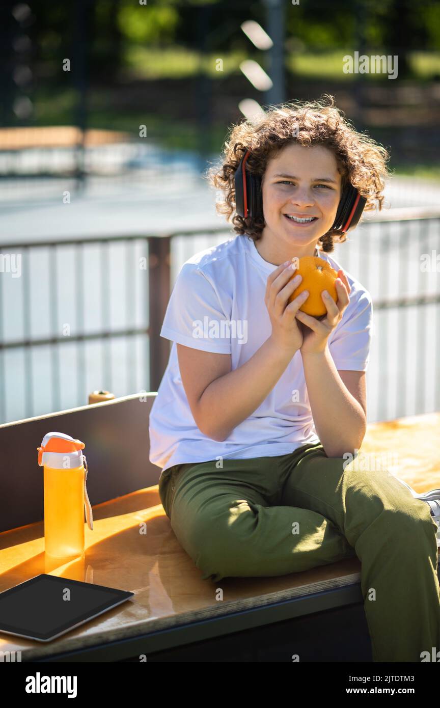 Teenager with a citrus fruit seated in an outdoor cafe Stock Photo