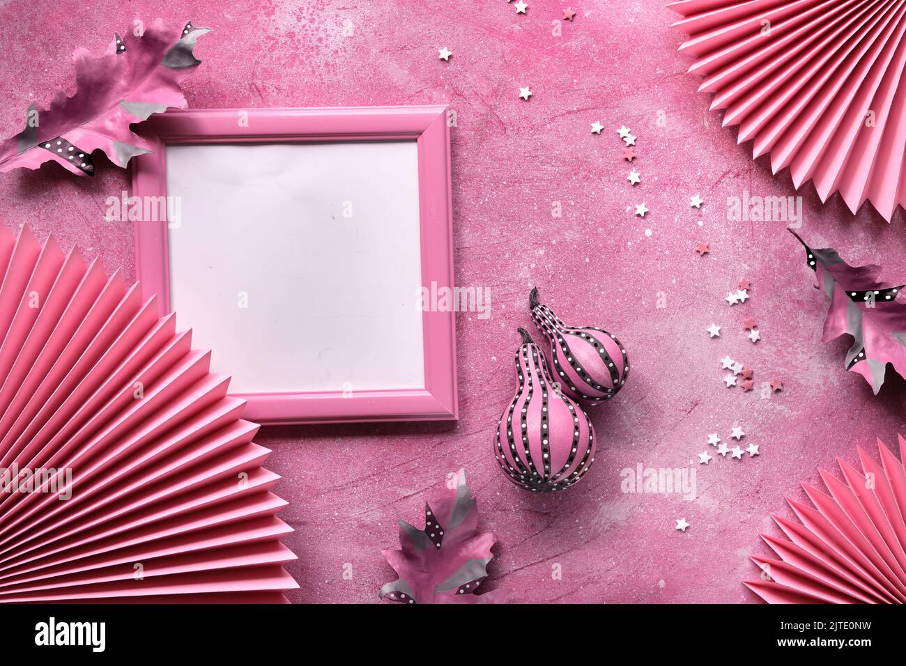 Pink blank picture frame with Autumn stripy pumpkins, Fall dry leaves. Paper fans, sugar sprinkles on pink textured monochromatic background. Stock Photo