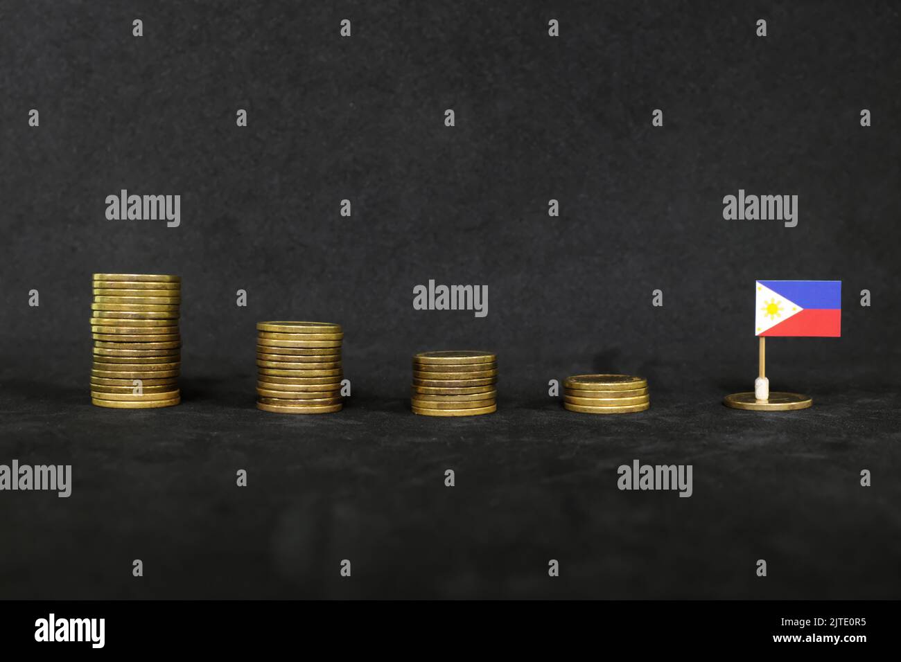 Philippines economic recession, financial crisis and peso depreciation concept. Philippine flag in decreasing stack of coins in dark black background. Stock Photo