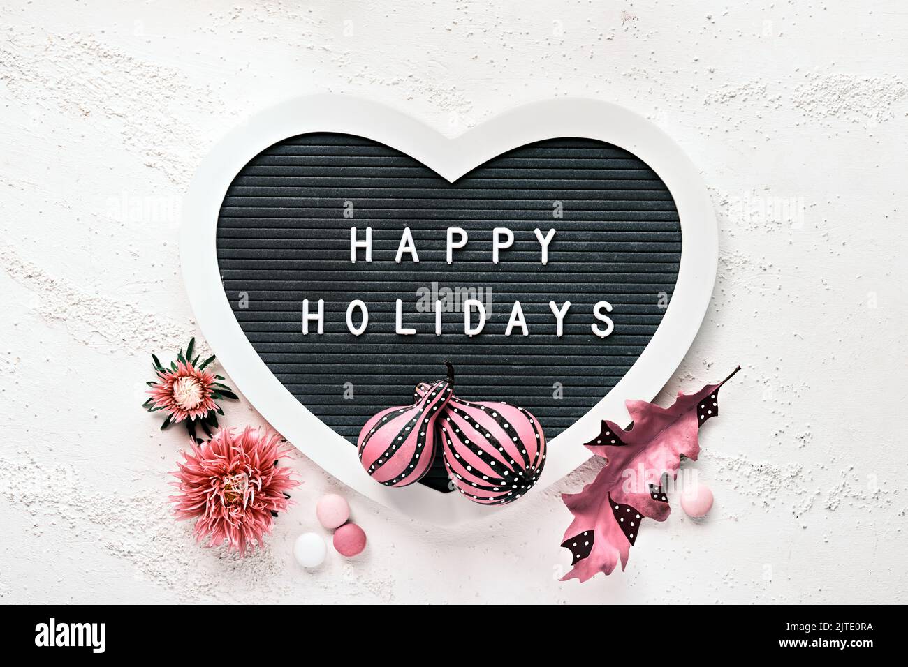 Heart shaped letter board with pink Fall decor. Text Happy Holidays on