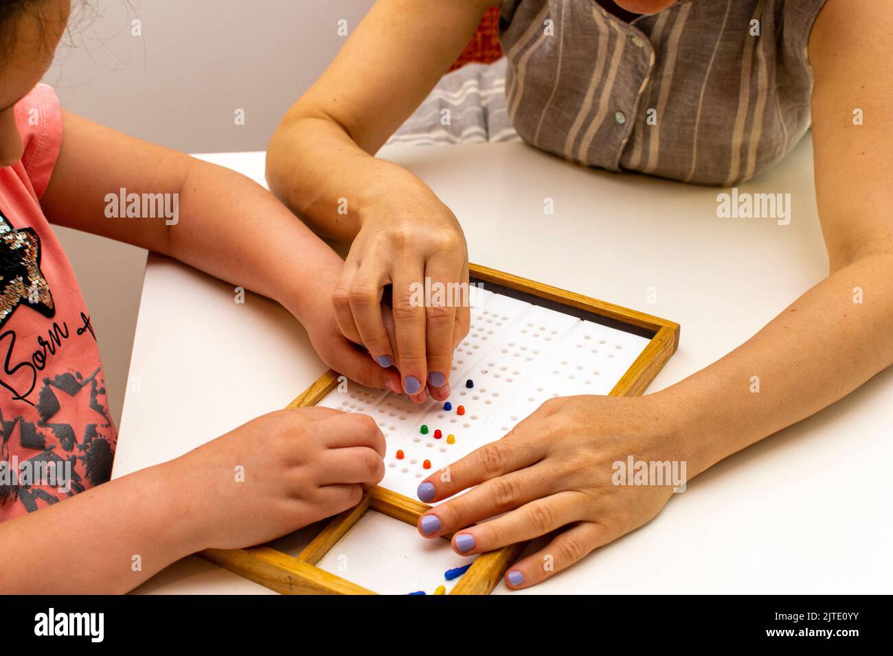 The hands of a girl and the hands of a teacher in close-up. Braille board for learning alphabet Stock Photo