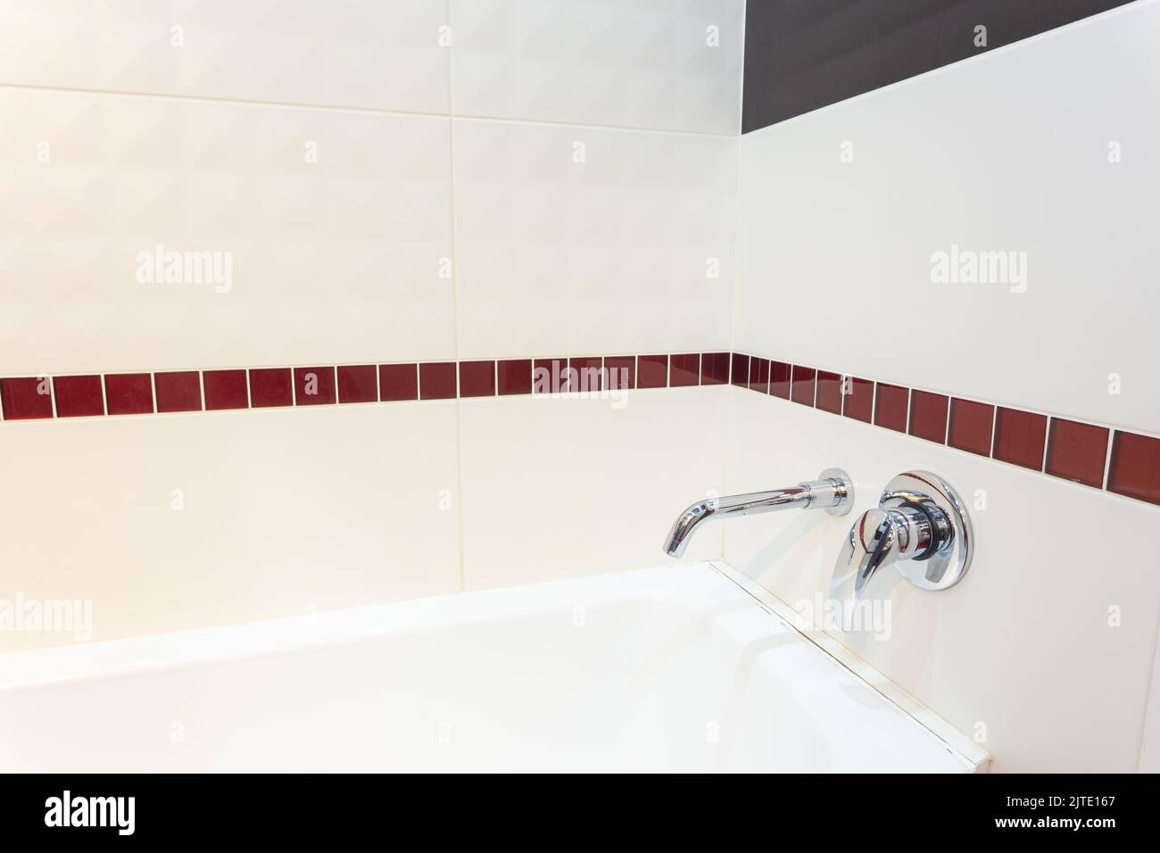 White acrylic bathtub with builtin wall mixer. The wall is lined with ceramic tiles Stock Photo