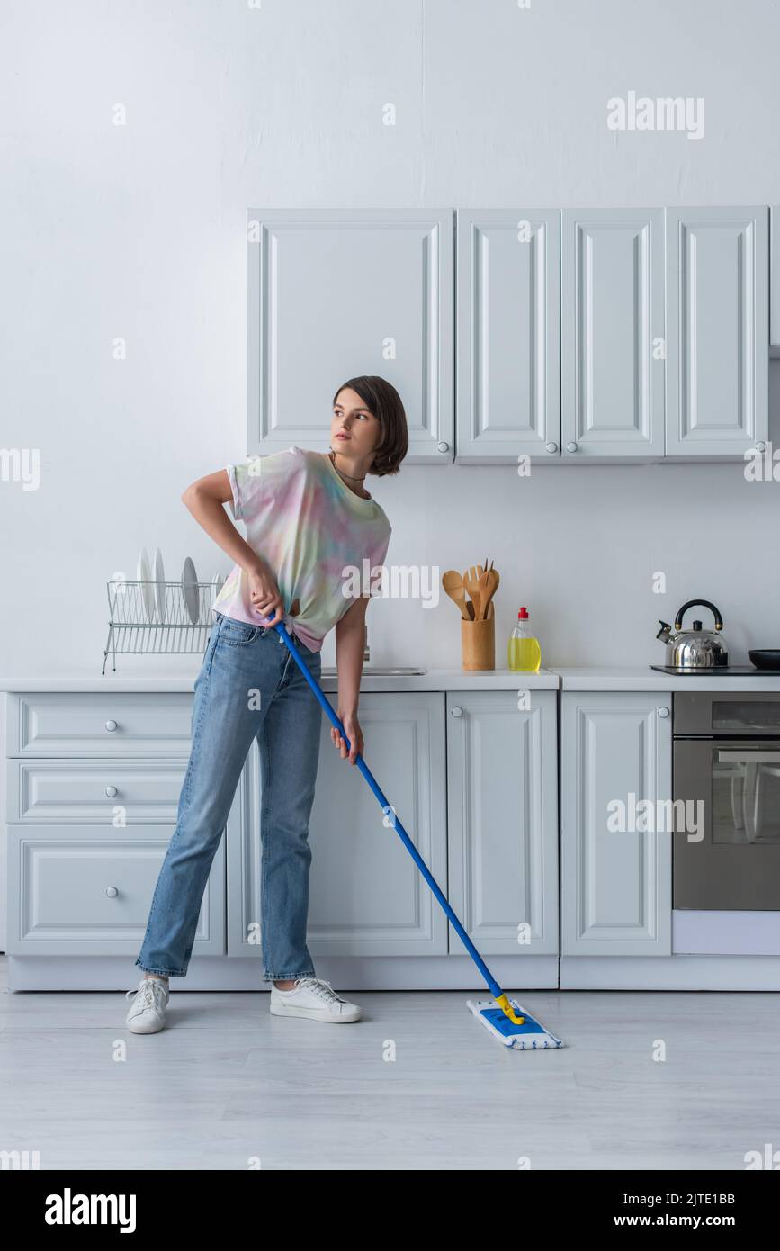 Young woman cleaning floor with mop in kitchen Stock Photo