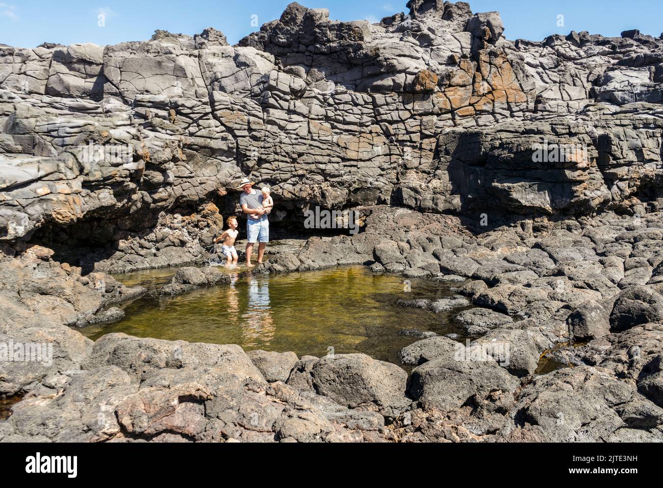 Father with two small sons enjoys his vacation by Charcones natural pools in Lanzarote, Canary Islands, Spain Stock Photo
