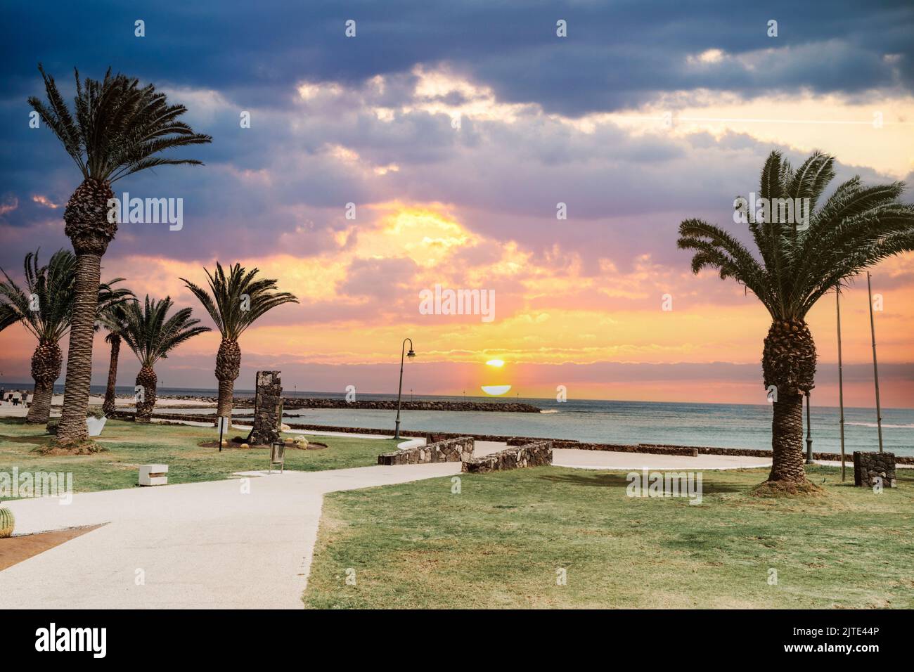 Sunset at the coast with palm trees by Los Charcos beach in Costa Teguise in Lanzarote, Canary Island, Spain Stock Photo