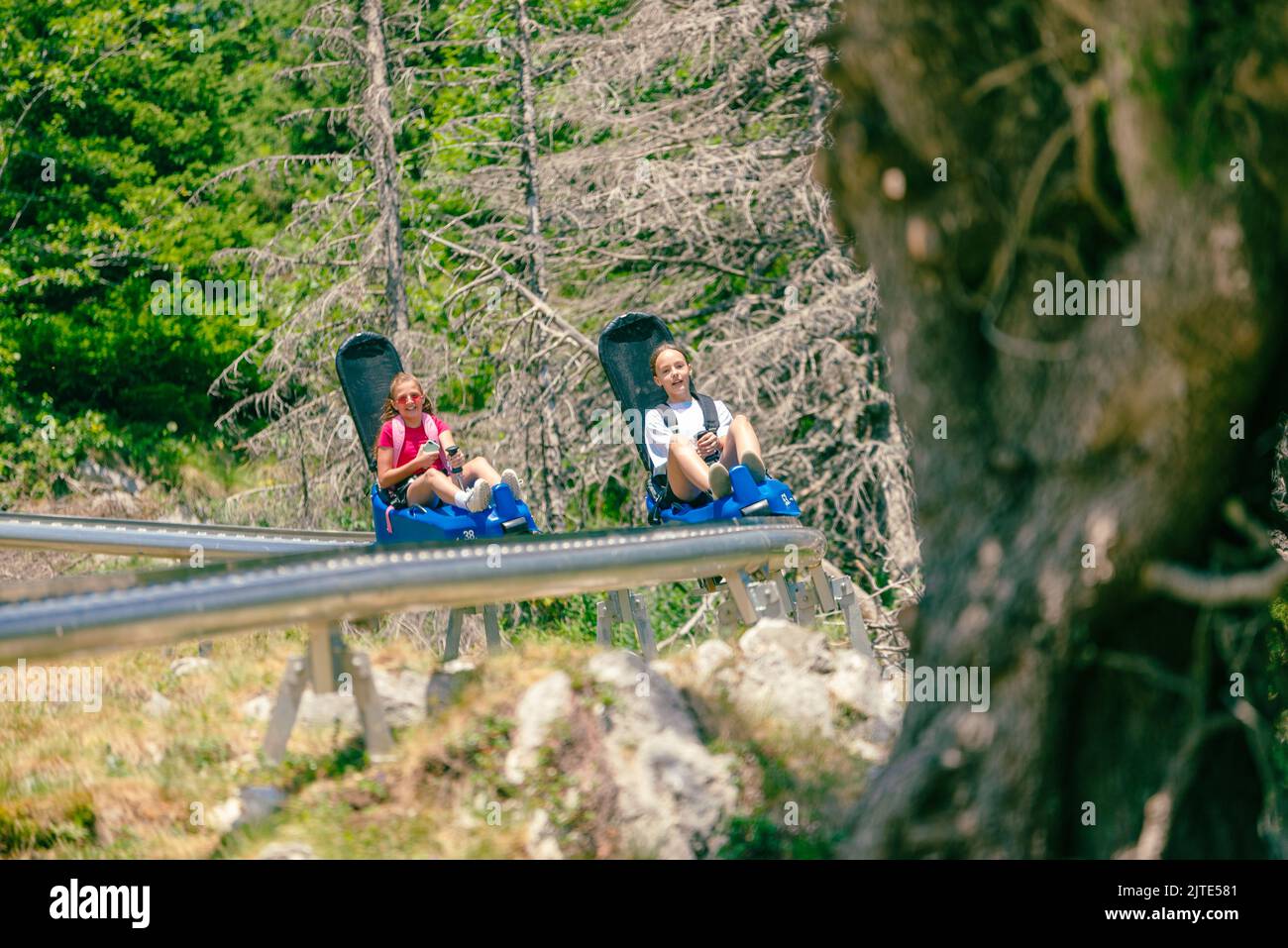 Girls ride a mountain roller coaster. Two mountain roller coasters. Tree ahead and a winding rail Stock Photo