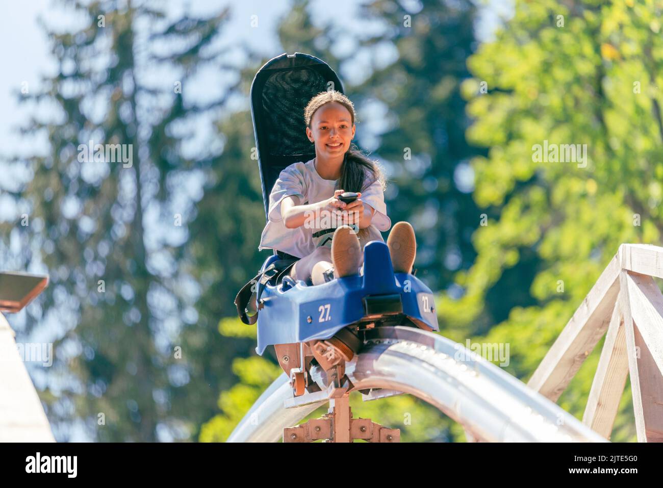 Dirl is going down a mountain with a roller coaster over a wooden bridge. Forest in background Stock Photo