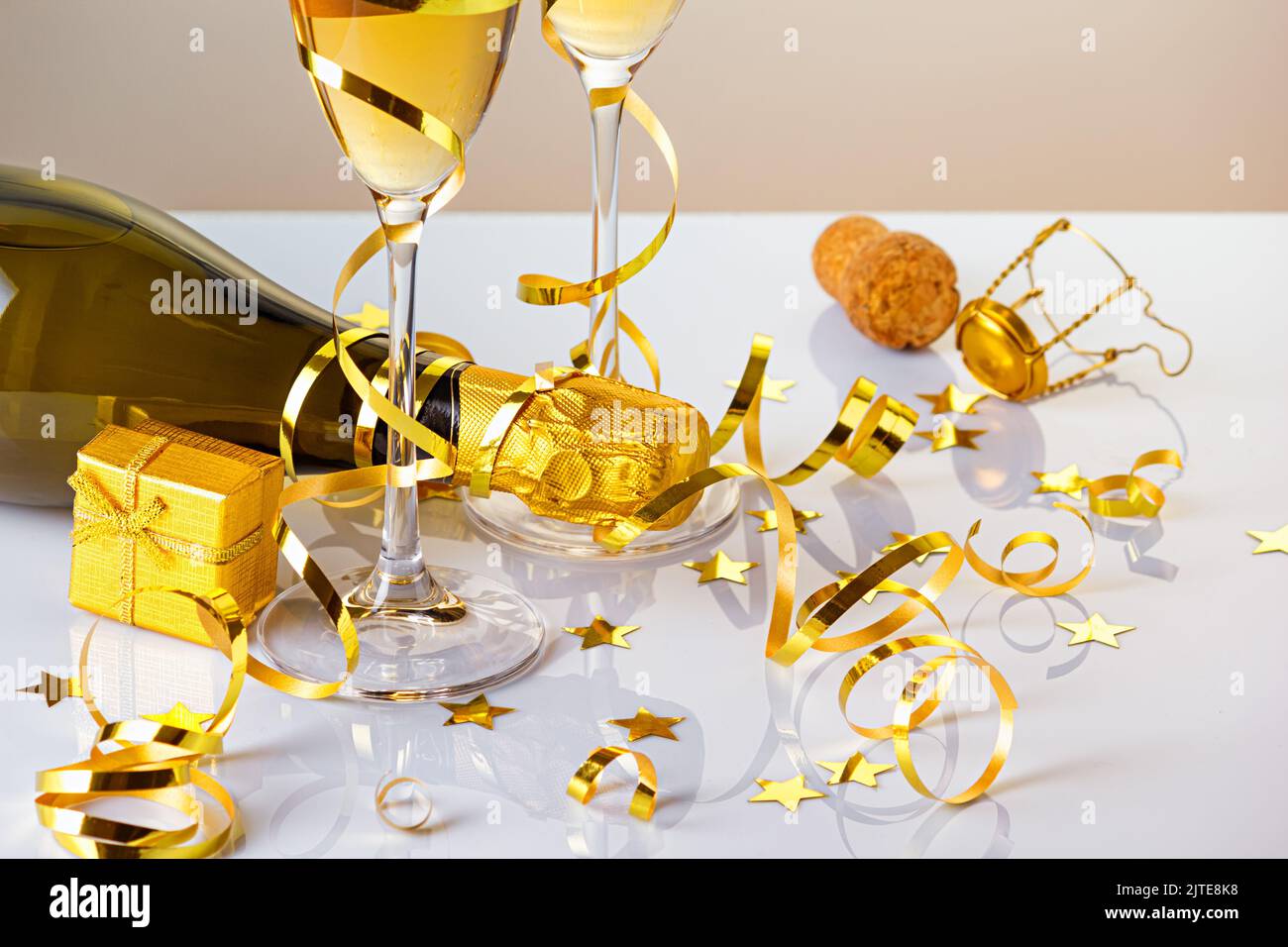 Two glasses of champagne with bottle, golden serpentine and a gift on a glossy surface. Selective focus Stock Photo