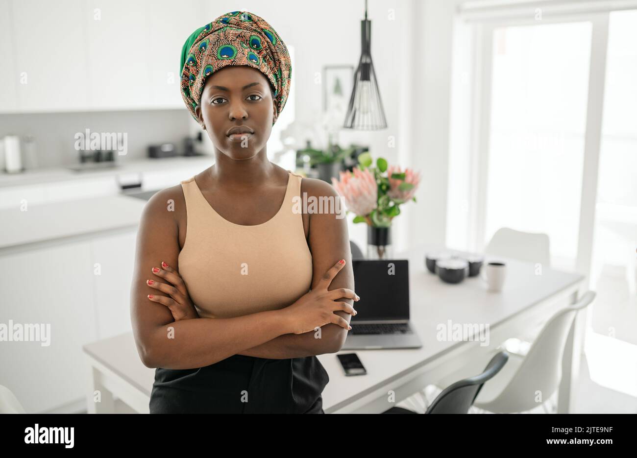 Portrait of a confident Black African woman with her arms crossed looking into the camera. Working from home and wearing a traditional headscarf Stock Photo