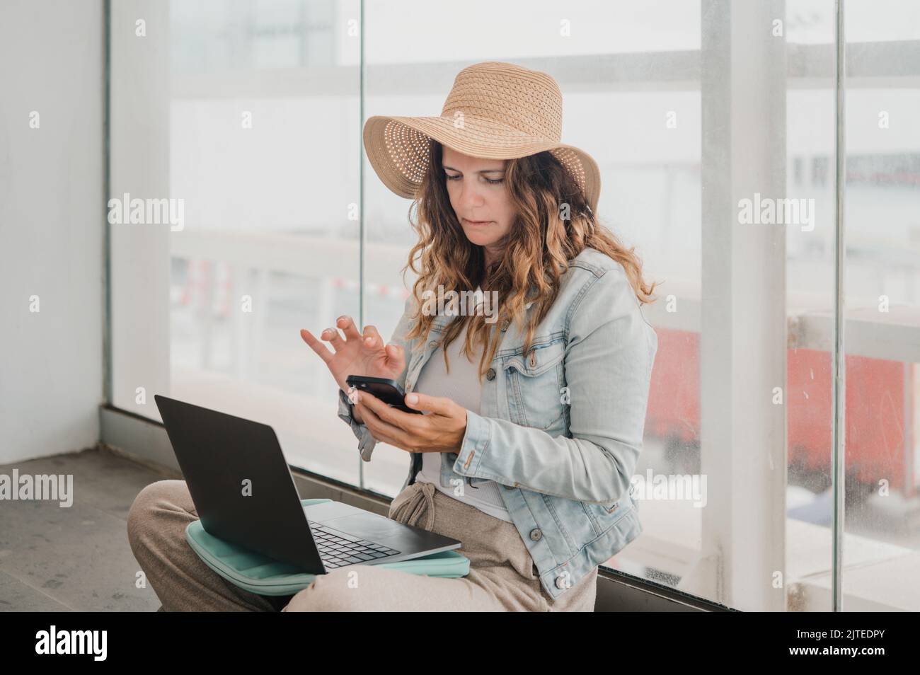 Freelancer with laptop using smartphone near window Stock Photo