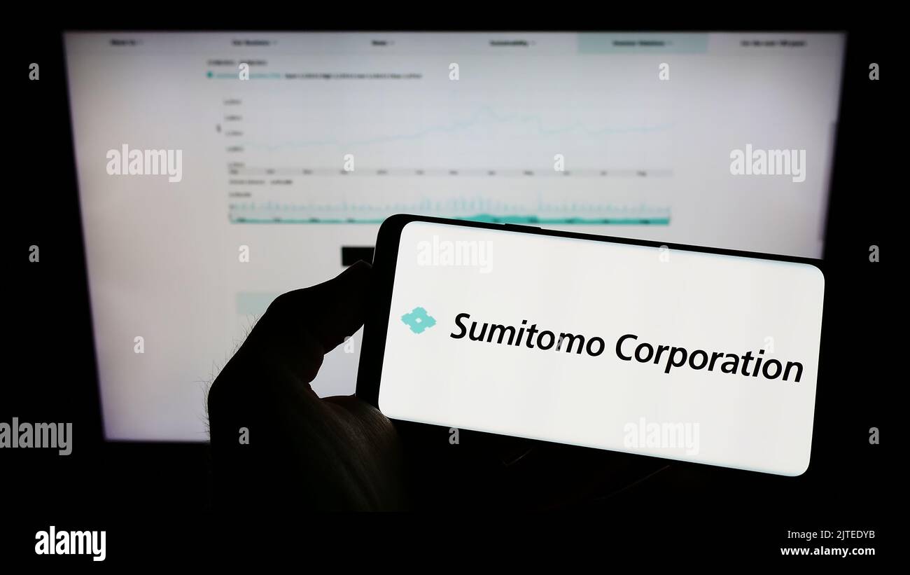 Person holding cellphone with logo of Japanese company Sumitomo Corporation on screen in front of business webpage. Focus on phone display. Stock Photo