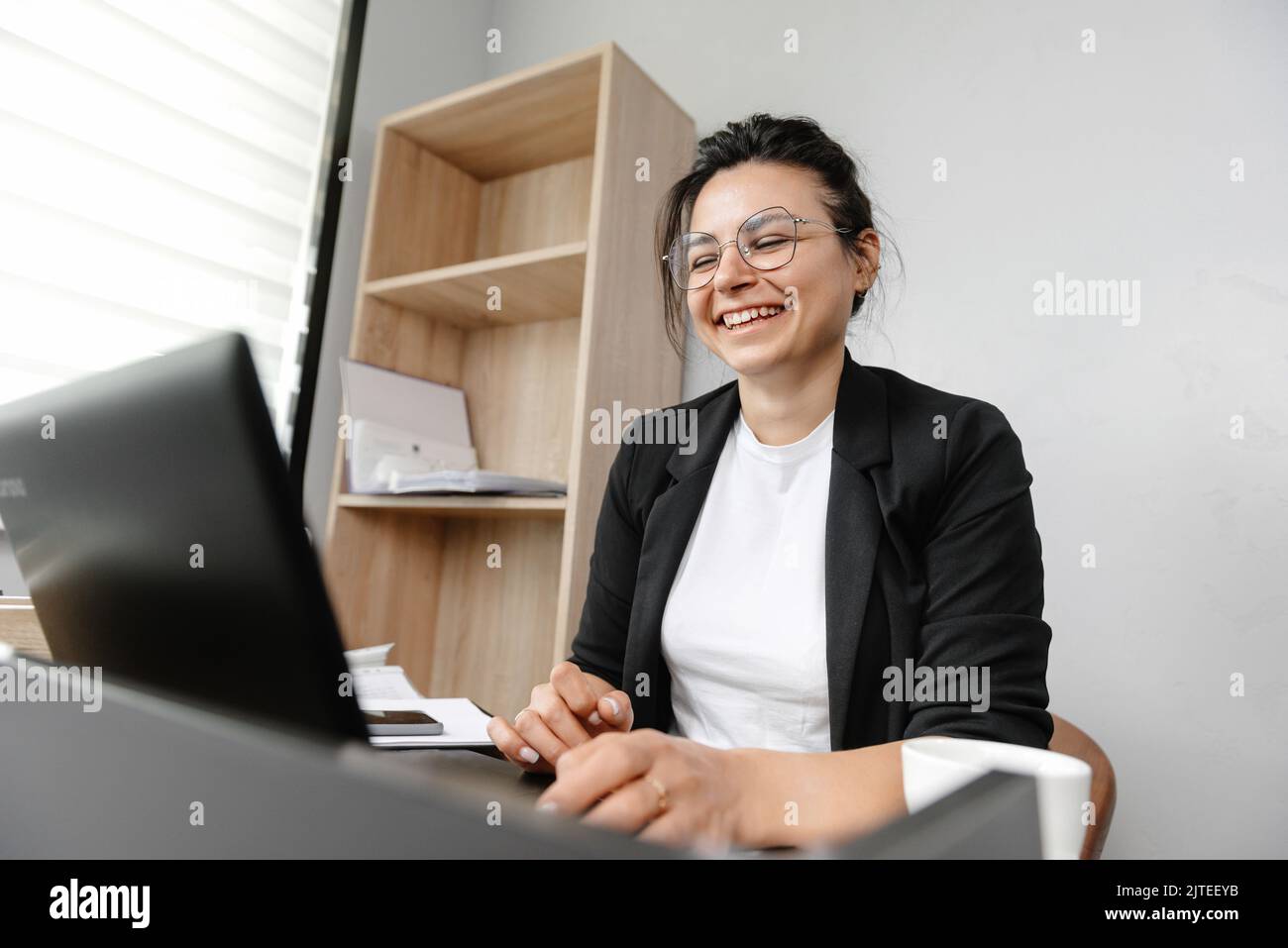 The girl in the office leads an online conference smiling and working at her laptop. Work in the office, girl office manager. Stock Photo