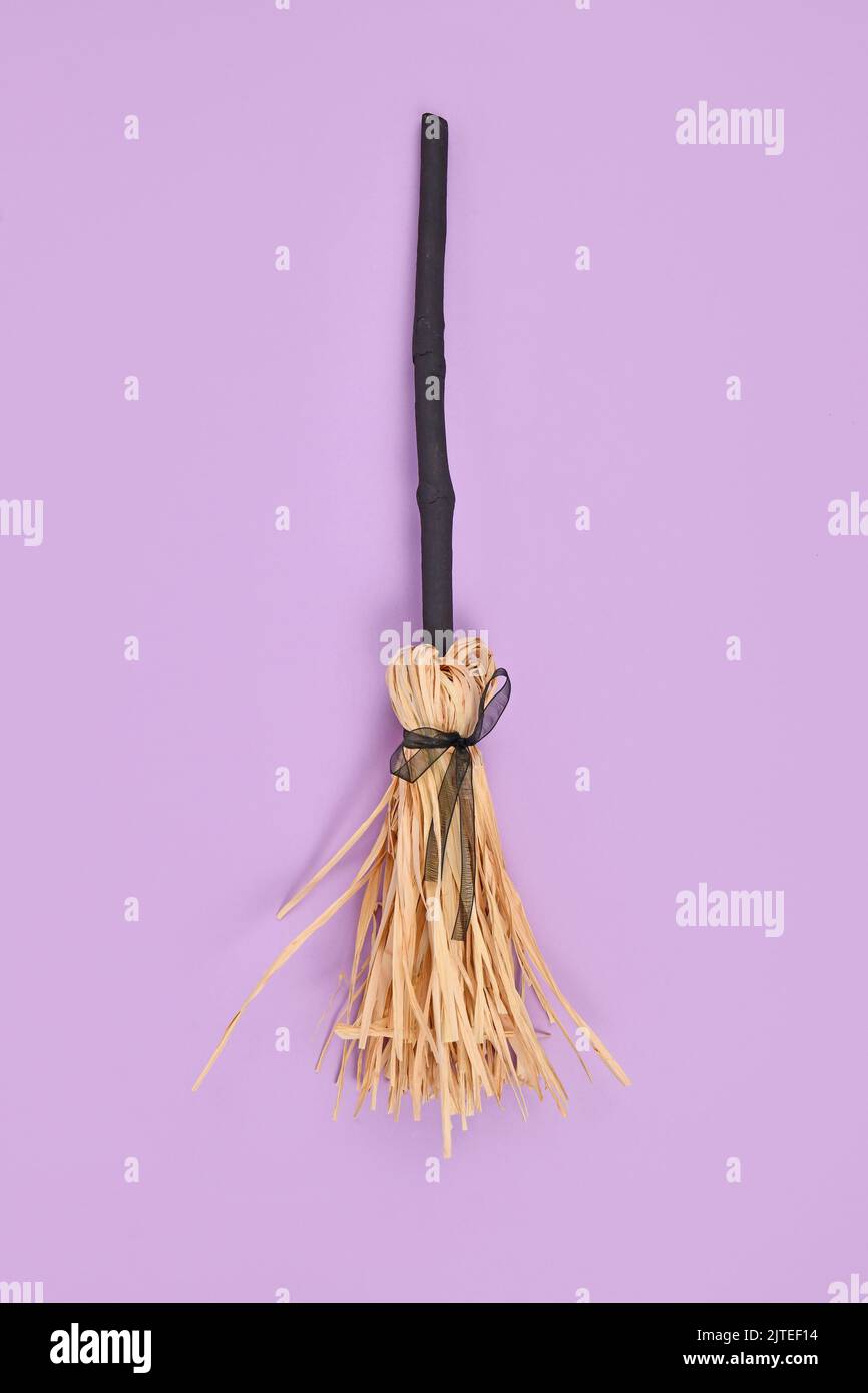 Witch broom with black twig and straw bristles on violet background Stock Photo