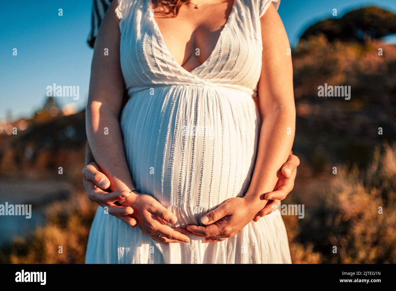 Pregnant woman with her partner holding her belly in the nature Stock Photo