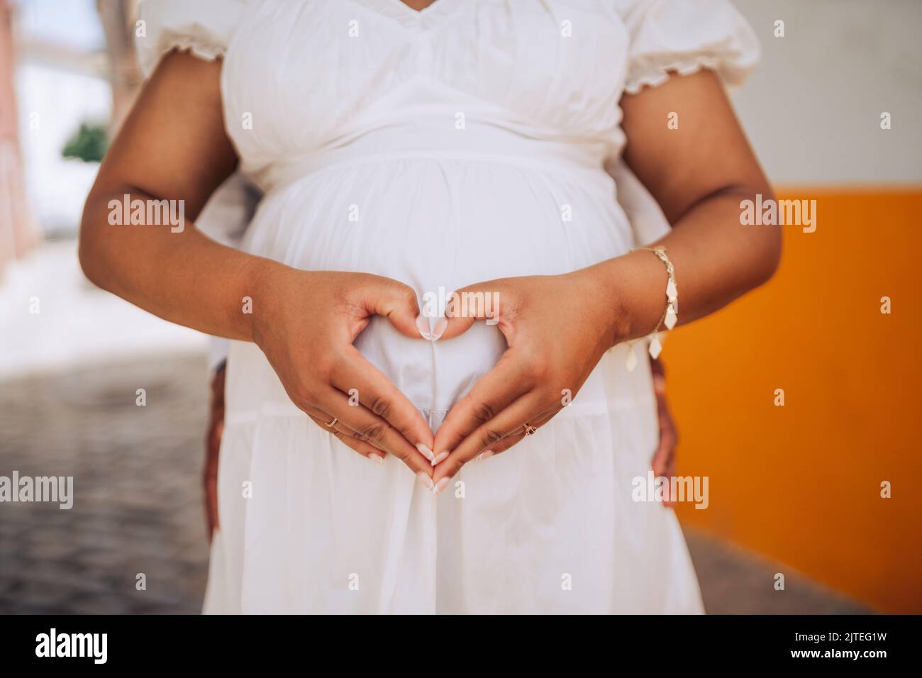 Pregnant woman showing heart shape at her tummy with her partner behind Stock Photo