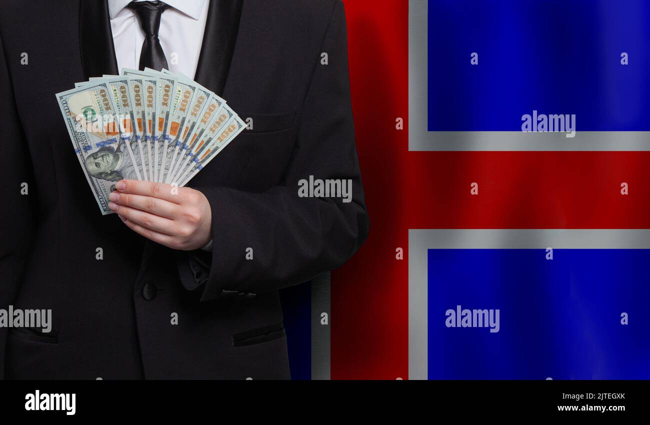 Icelandic businessman holds US 100 dollar bills against flag of Iceland background Stock Photo