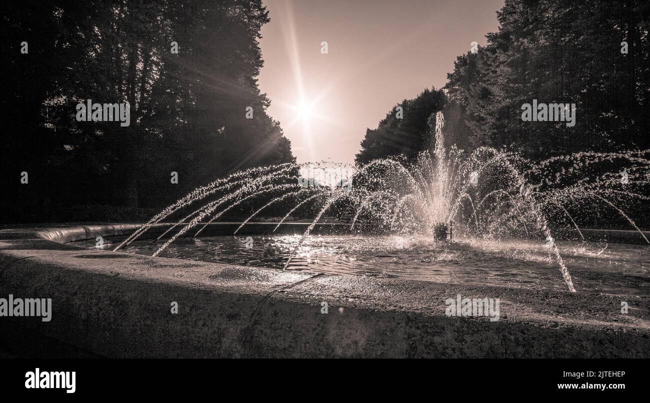 Fountain with fountain, trees and sky with sun star in background Stock Photo