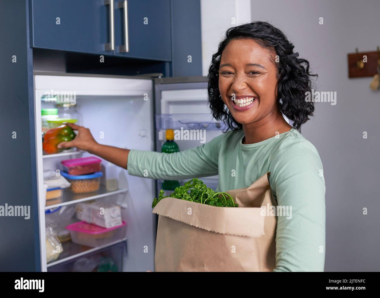 A young multi-racial woman unpacks her grocery shopping into the refrigerator Stock Photo