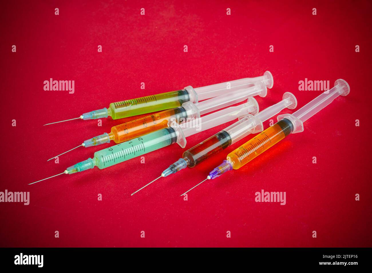 Closeup bunch of colorful syringes isolated on red background. Drug