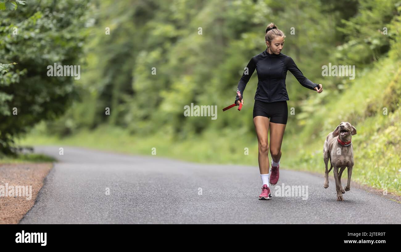 Young female holding leash releases her dog on an empty road during
