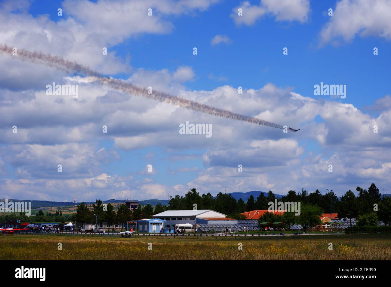 Single engine small airplane making acrobatic maneuvers at cloudy sky, with smoke on tail Stock Photo