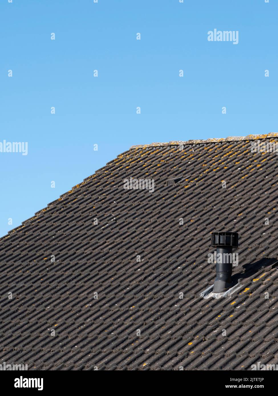 Black roof with pipe for the ventilation system and the background is a beautiful light blue sky Stock Photo