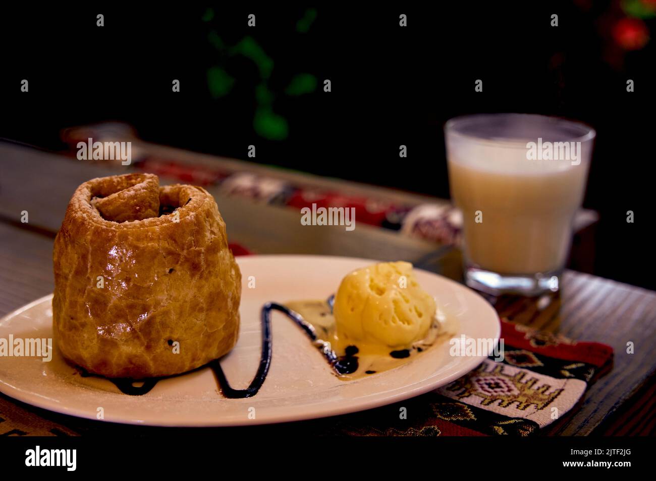 Fultu with ice cream. Puff pastry roll with apples and nuts on a white ceramic plate and a glass of ayran. Crimean Tatar cuisine. Stock Photo