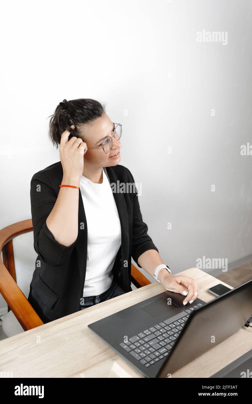 Serious thoughtful young businesswoman economist pondering in the office, wearing a jacket and T-shirt and glasses Stock Photo