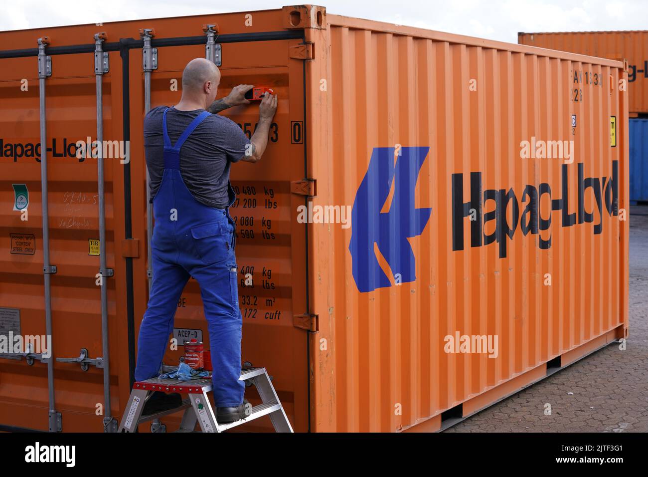 30 August 2022, Hamburg: Employee Marius Paluch attaches a live tracking  device to a Hapag-Lloyd standard container at the CMR (Container  Maintenance Repair) depot in the port. The first of these devices