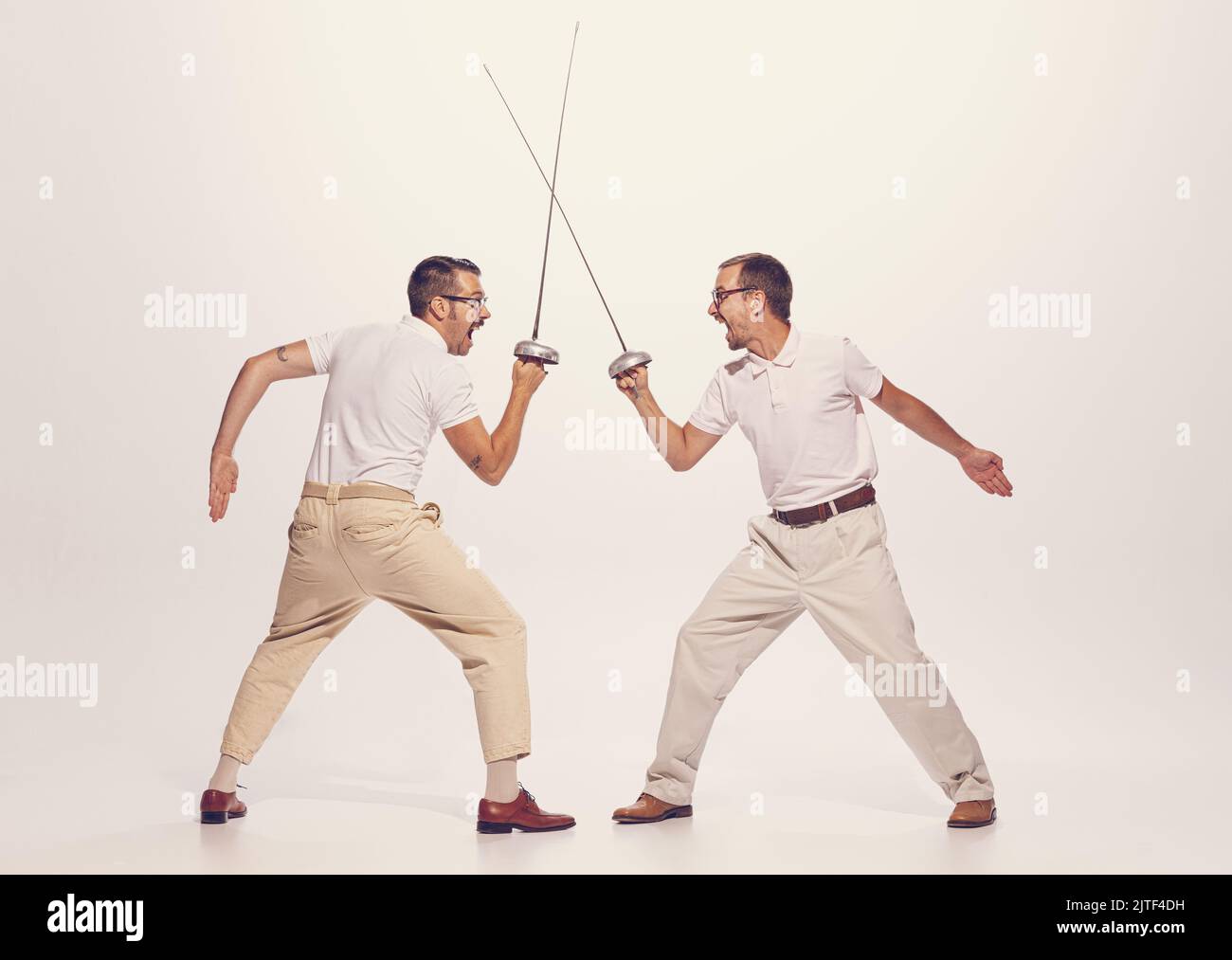 Portrait of two men in a suit fighting with swords isolated over grey ...