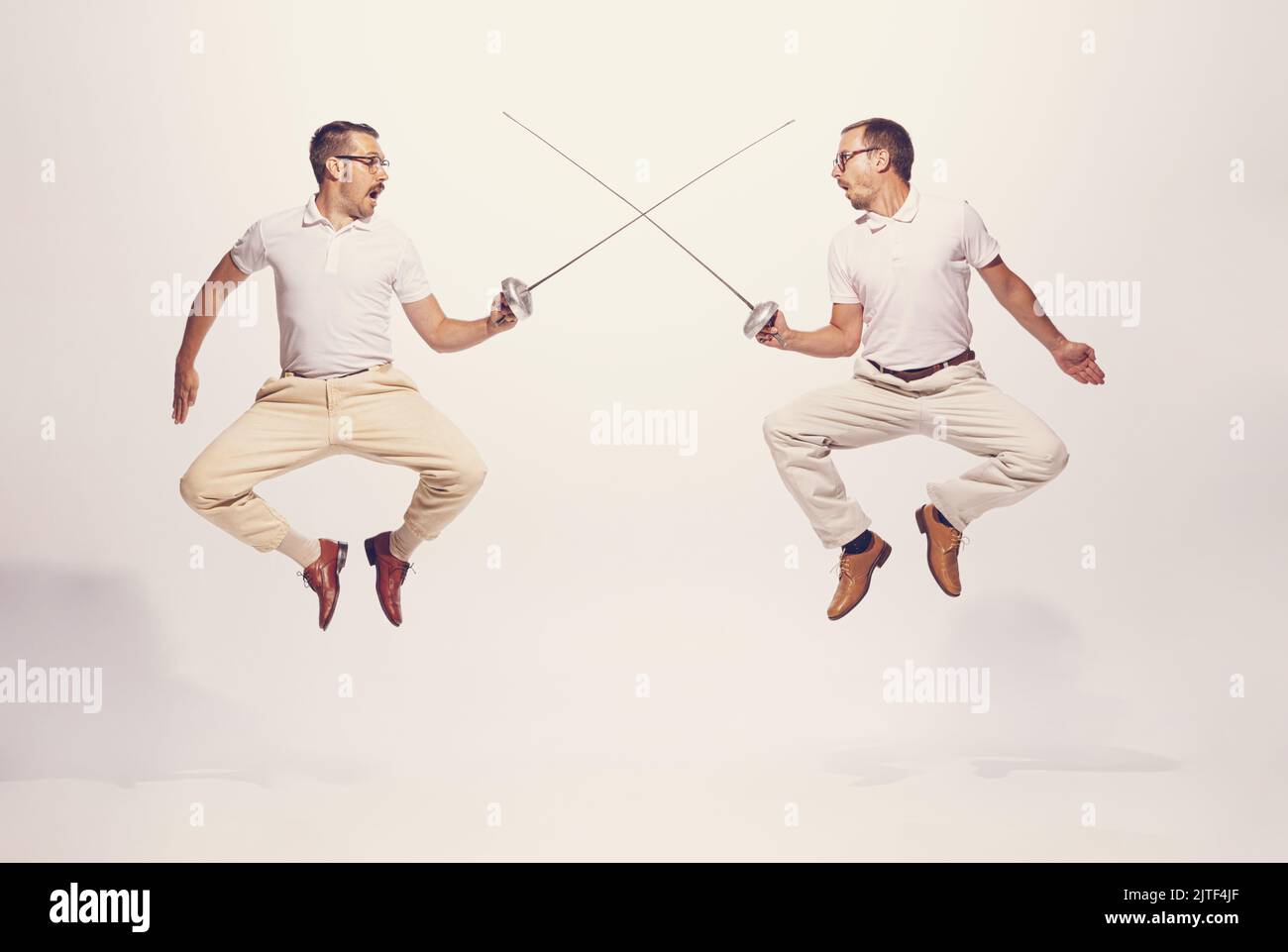 Portrait of two men in a suit fighting with swords in a jump isolated ...