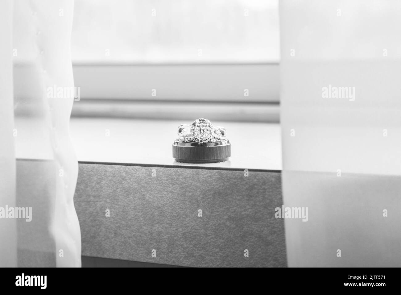 Male and female wedding rings stacked on a window ledge with sheer curtains. Stock Photo