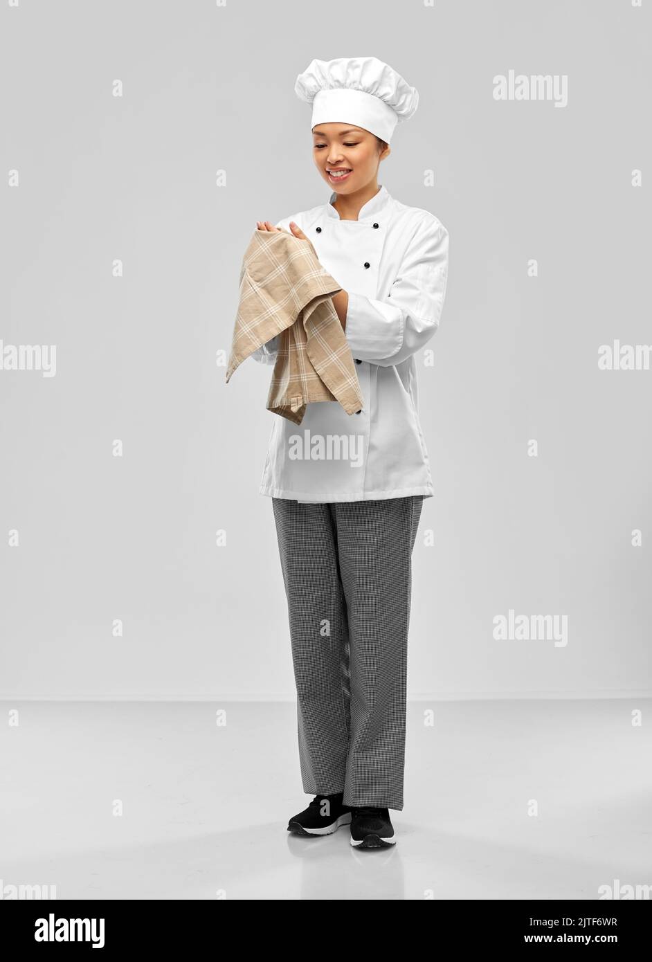 smiling female chef in jacket with kitchen towel Stock Photo