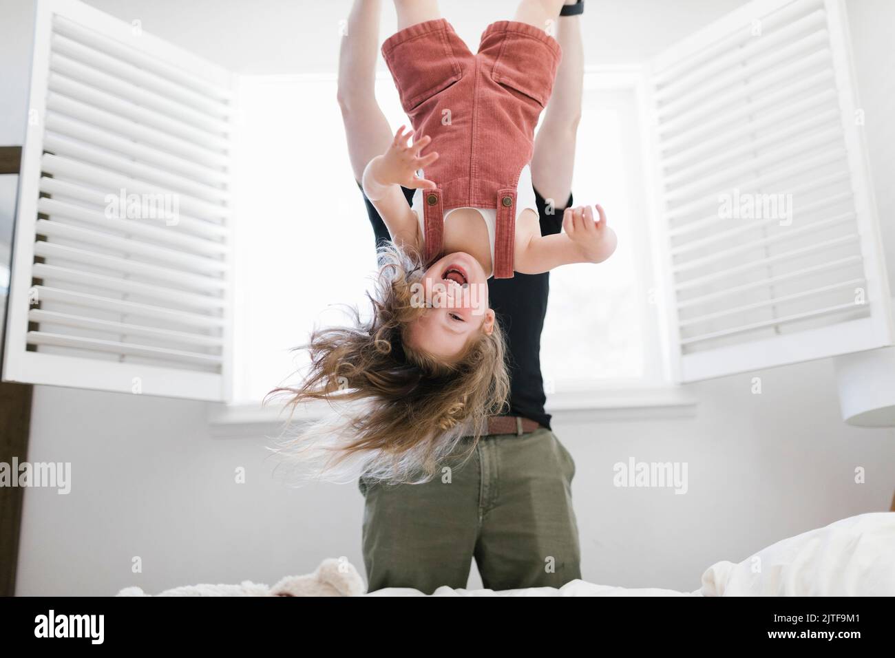 Father swinging daughter (2-3) playfully in bedroom Stock Photo