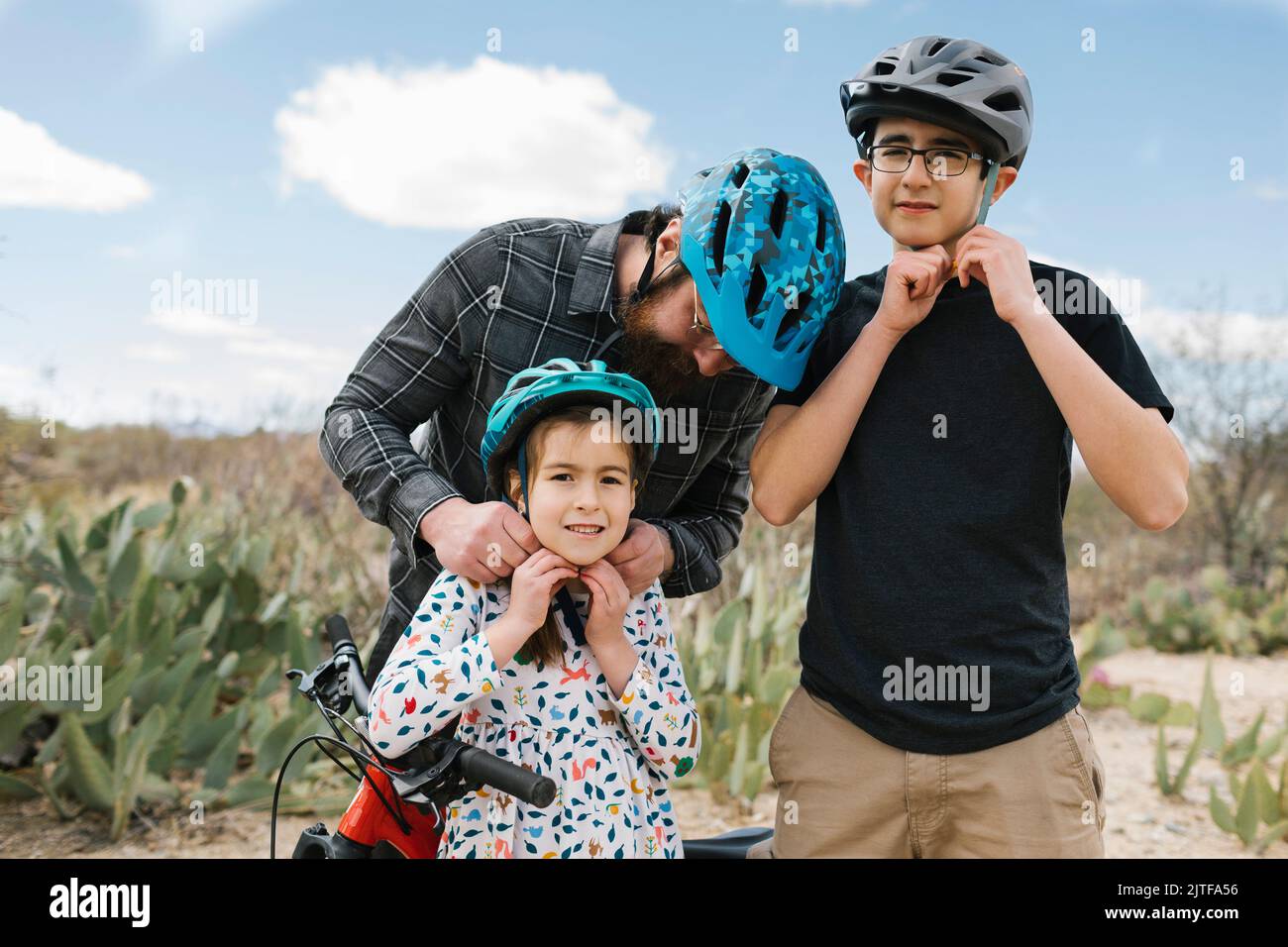 Father and children (8-9, 14-15) adjusting bike helmets Stock Photo