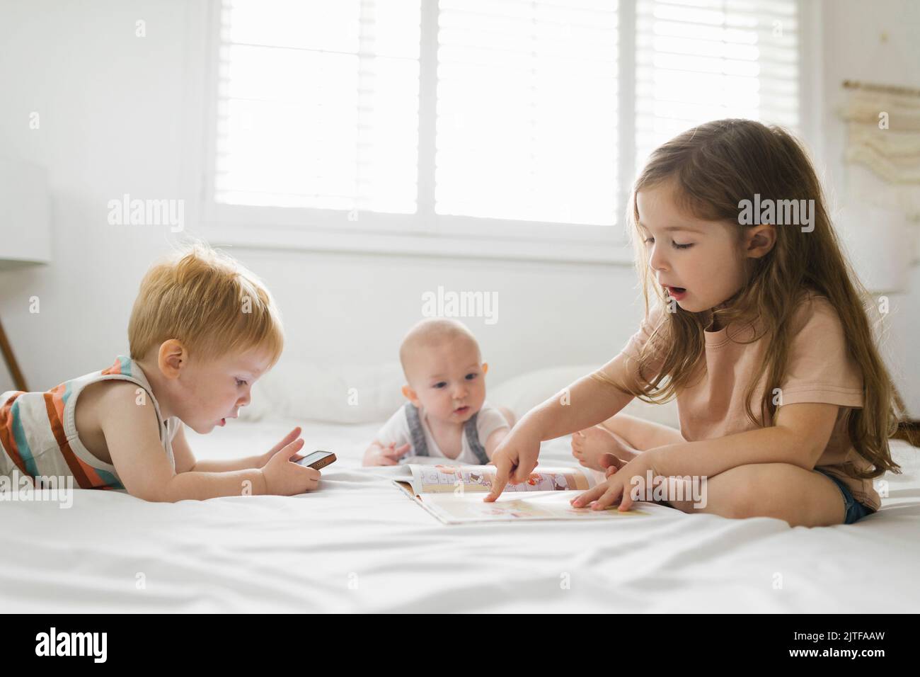 Siblings (6-11 months, 2-3) reading and using phone Stock Photo