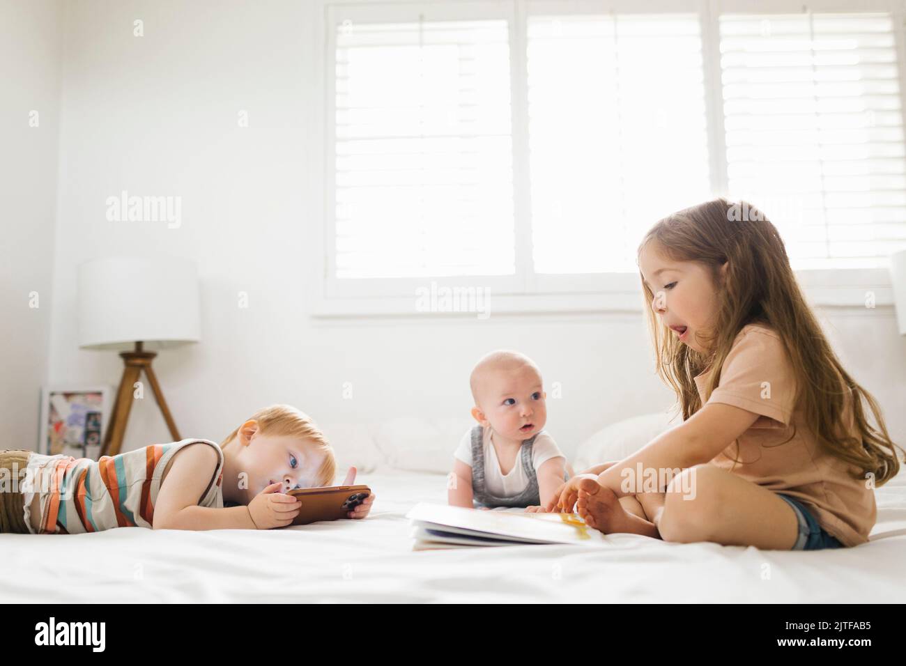 Siblings (6-11 months, 2-3) reading and using phone Stock Photo