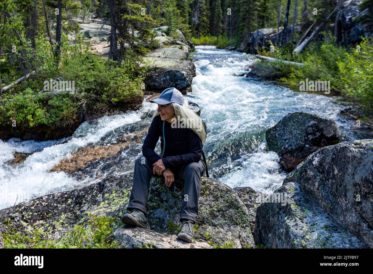 United States, Idaho, Stanley, Senior blonde woman hiking by rushing stream in mountains near Sun Valley Stock Photo