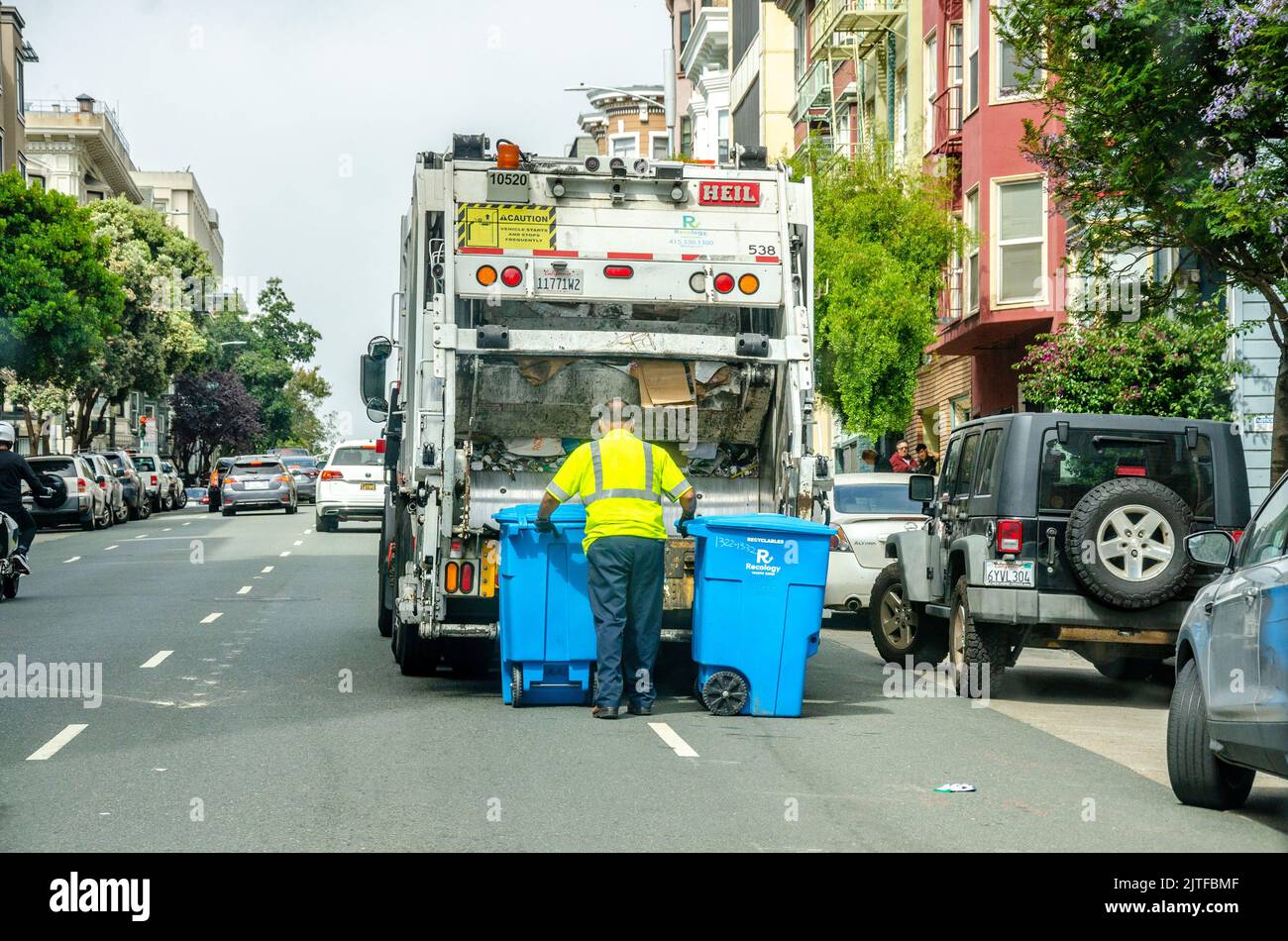 A man empties blue wheelie bins containing waste paper into the back of a garbage truck or bin lorry on a street in San Francisco, California, USA Stock Photo