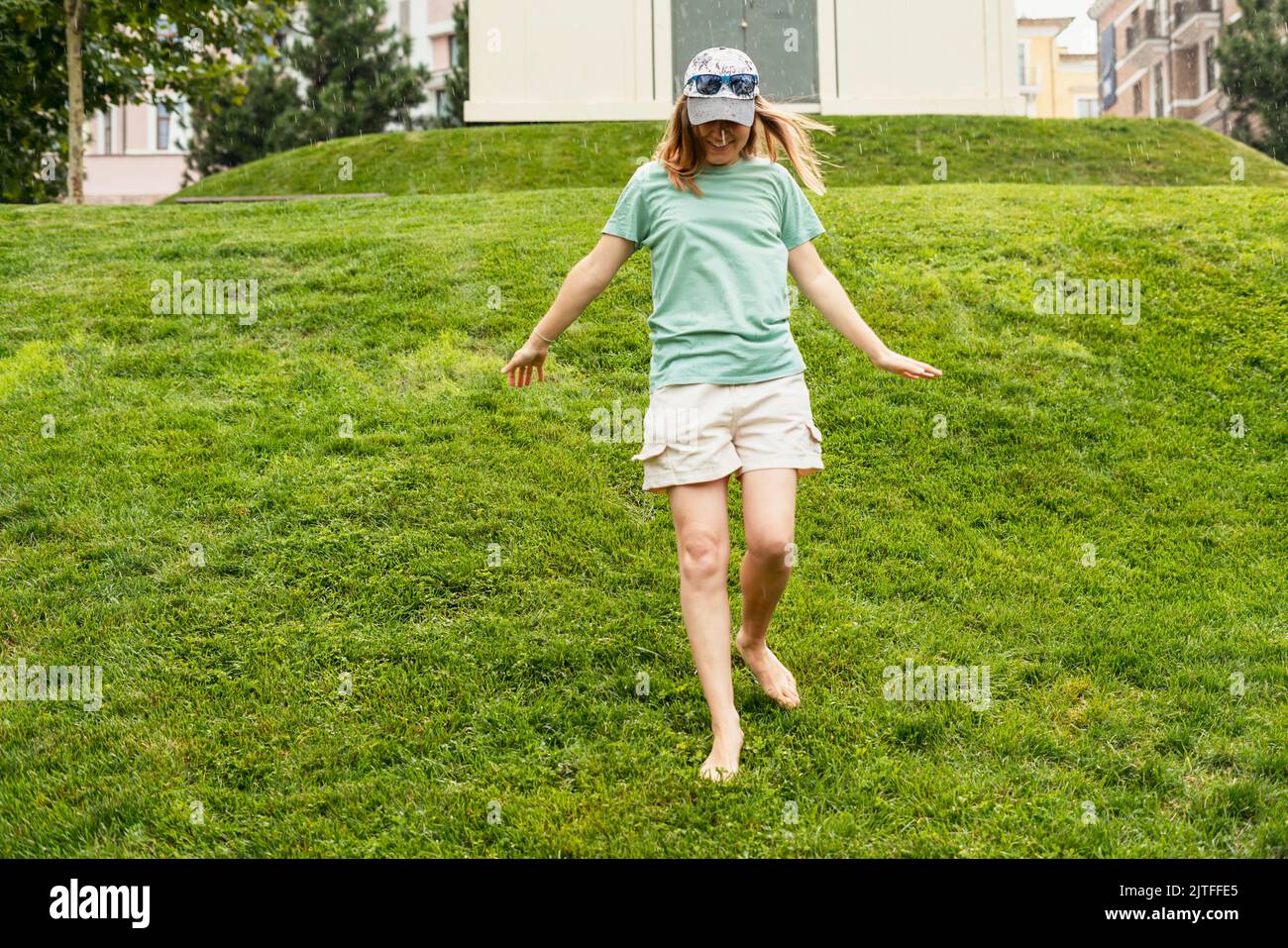 happy young woman barefoot walking on green grass lawn enjoying the warm rain in Summer enjoying nature feeling Stock Photo
