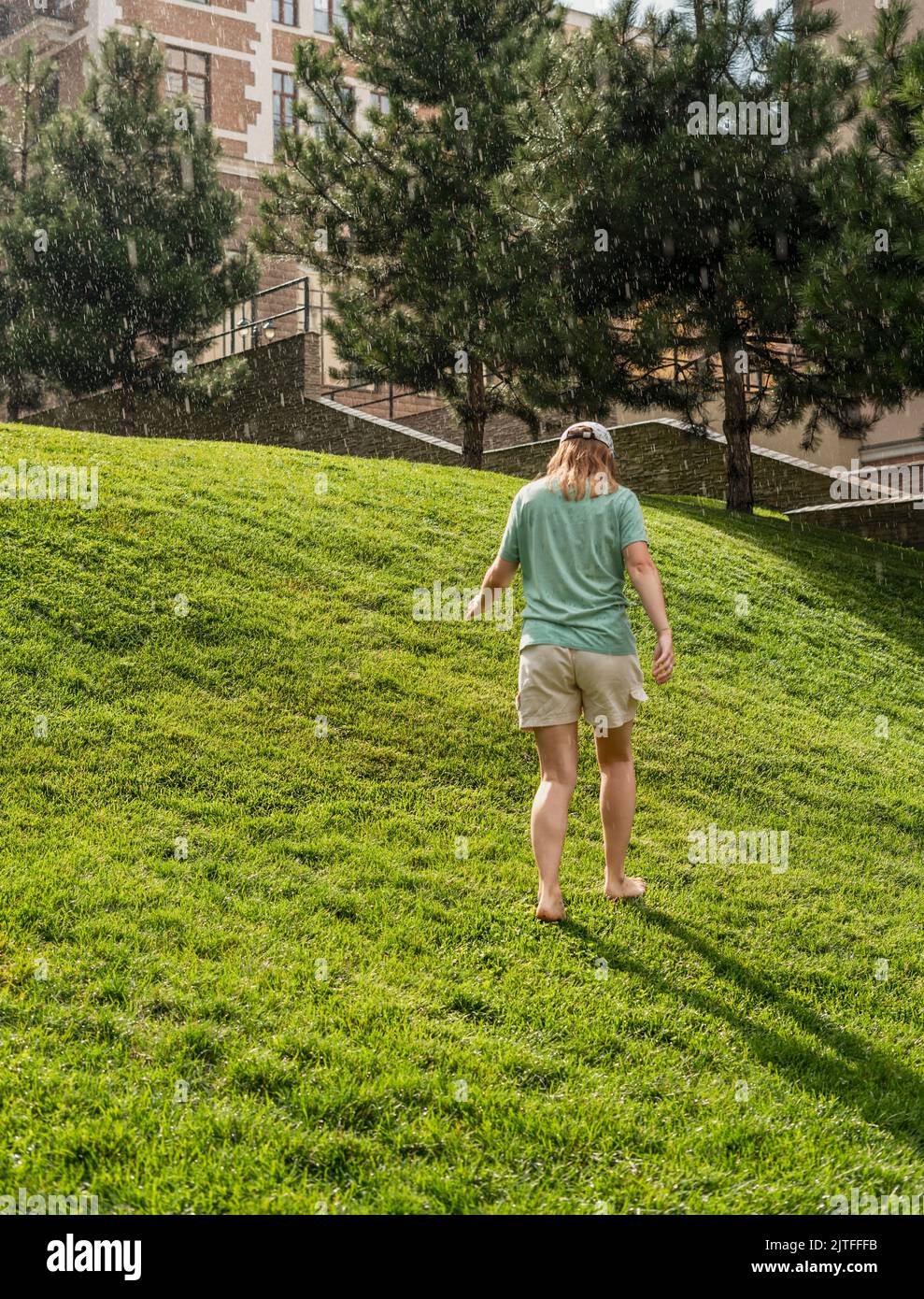 happy young woman barefoot walking on green grass lawn enjoying the warm rain in Summer enjoying nature feeling Stock Photo