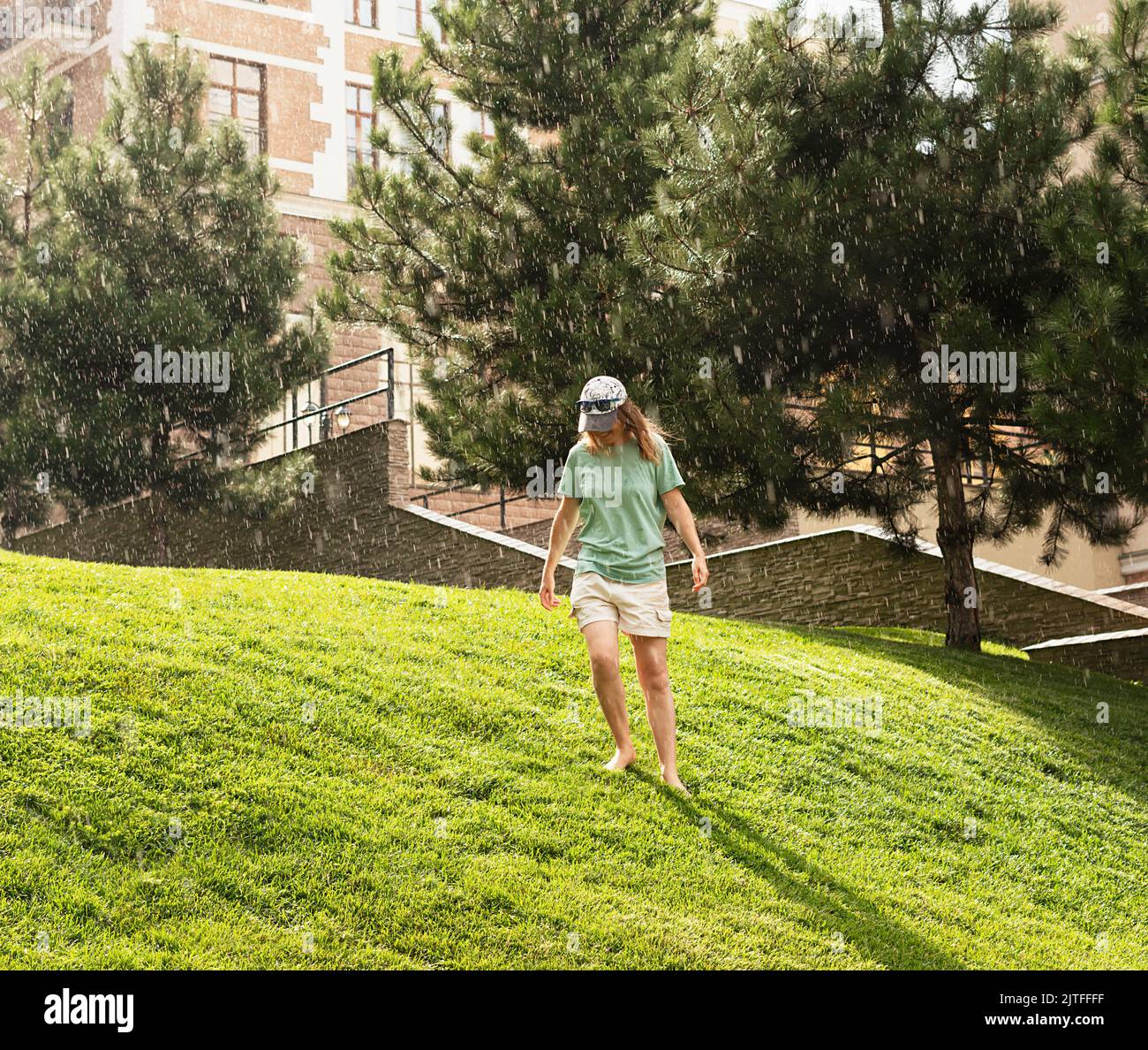 happy young woman barefoot walking on green grass lawn enjoying the warm rain in Summer enjoying nature feeling Stock Photo