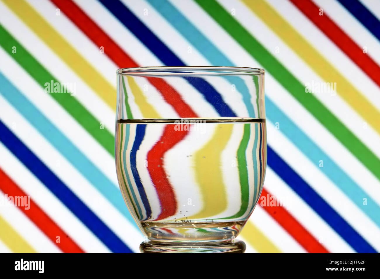 Ilusión óptica creada mediante la refracción de la luz con un vaso de agua y lineas diagonales de colores Stock Photo