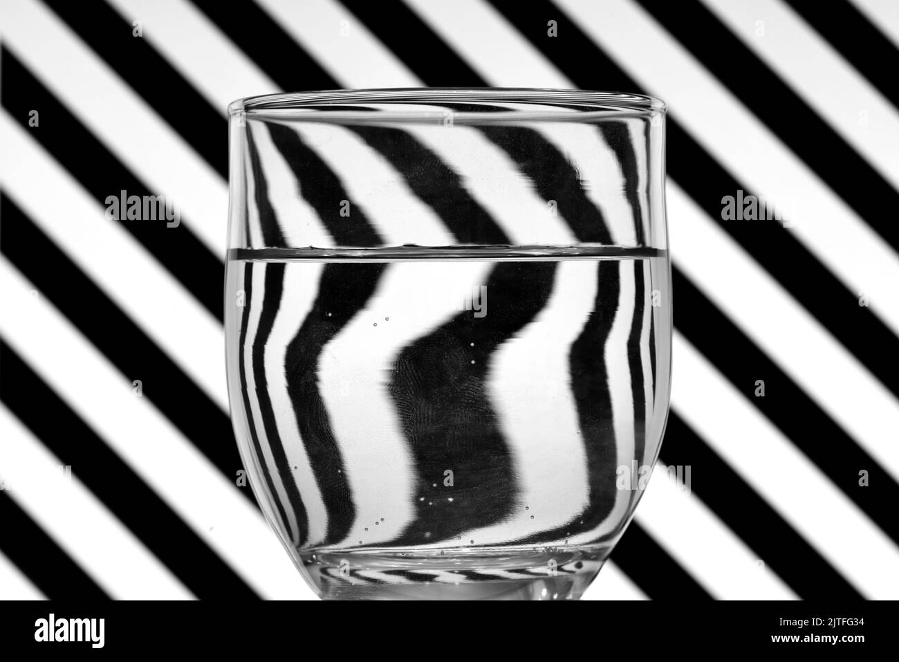 Ilusión óptica creada mediante la refracción de la luz, lineas oblicuas en blanco y negro reflejadas en un vaso de agua Stock Photo