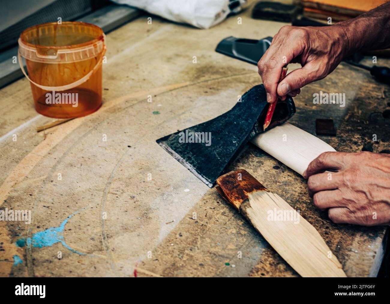 Unrecognizable person making handmade ax. Closeup old senior male hand creating wooden handle for axe. Mature man working in carpentry workshop concep Stock Photo