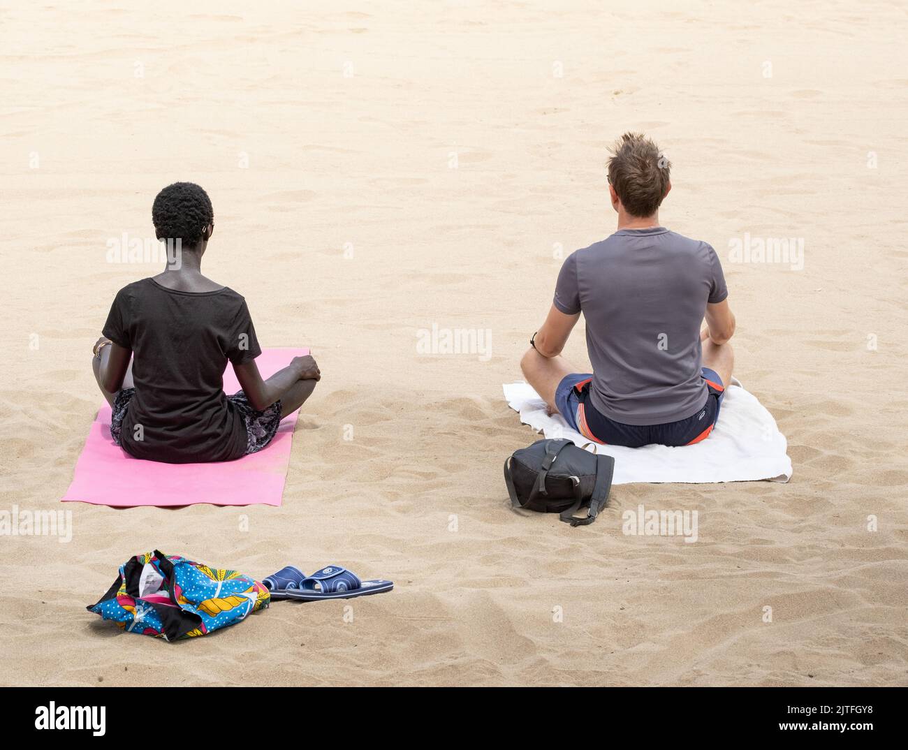 Mixed race couple performing yoga, meditation on beach. Stock Photo