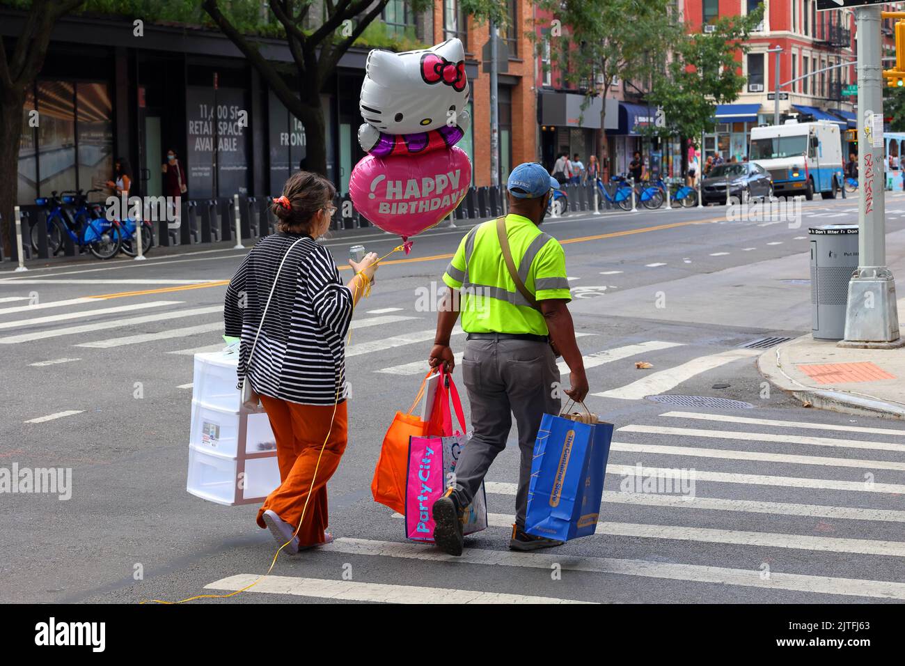 People walking down a street with a Hello Kitty happy birthday balloon and party supplies in the East Village neighborhood in Manhattan, New York City Stock Photo