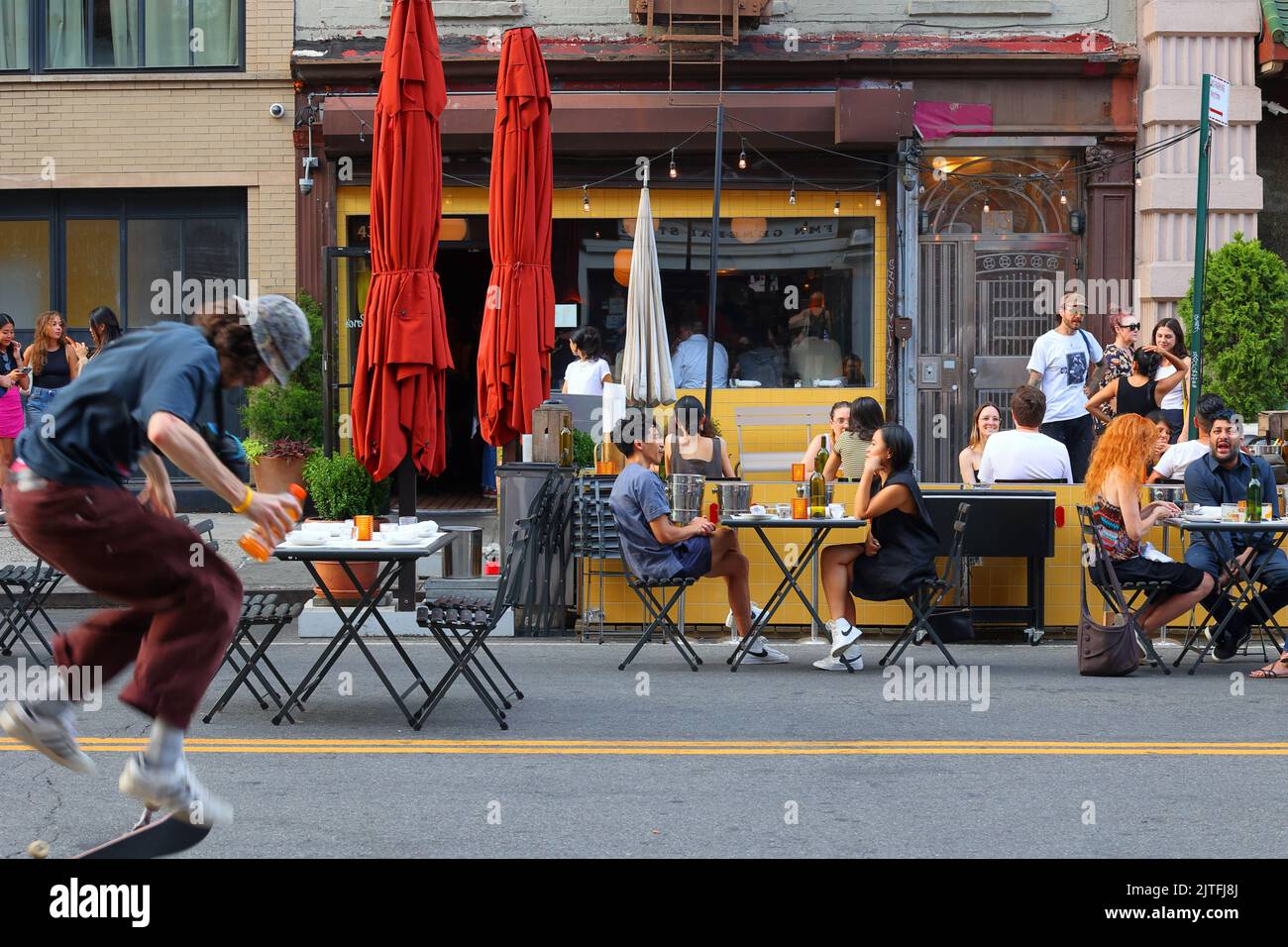 Skateboarder and diners outside Cervo's, 43 Canal St, in Manhattan's gentrifying 'Dimes Square' Chinatown/Lower East Side, New York. Stock Photo